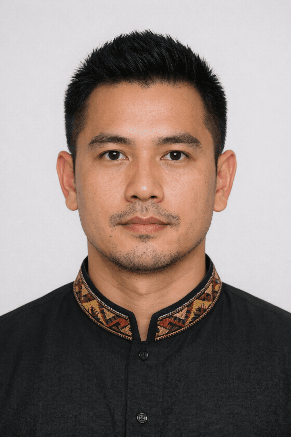 Man with short black hair wearing a black shirt with a patterned, embroidered collar.